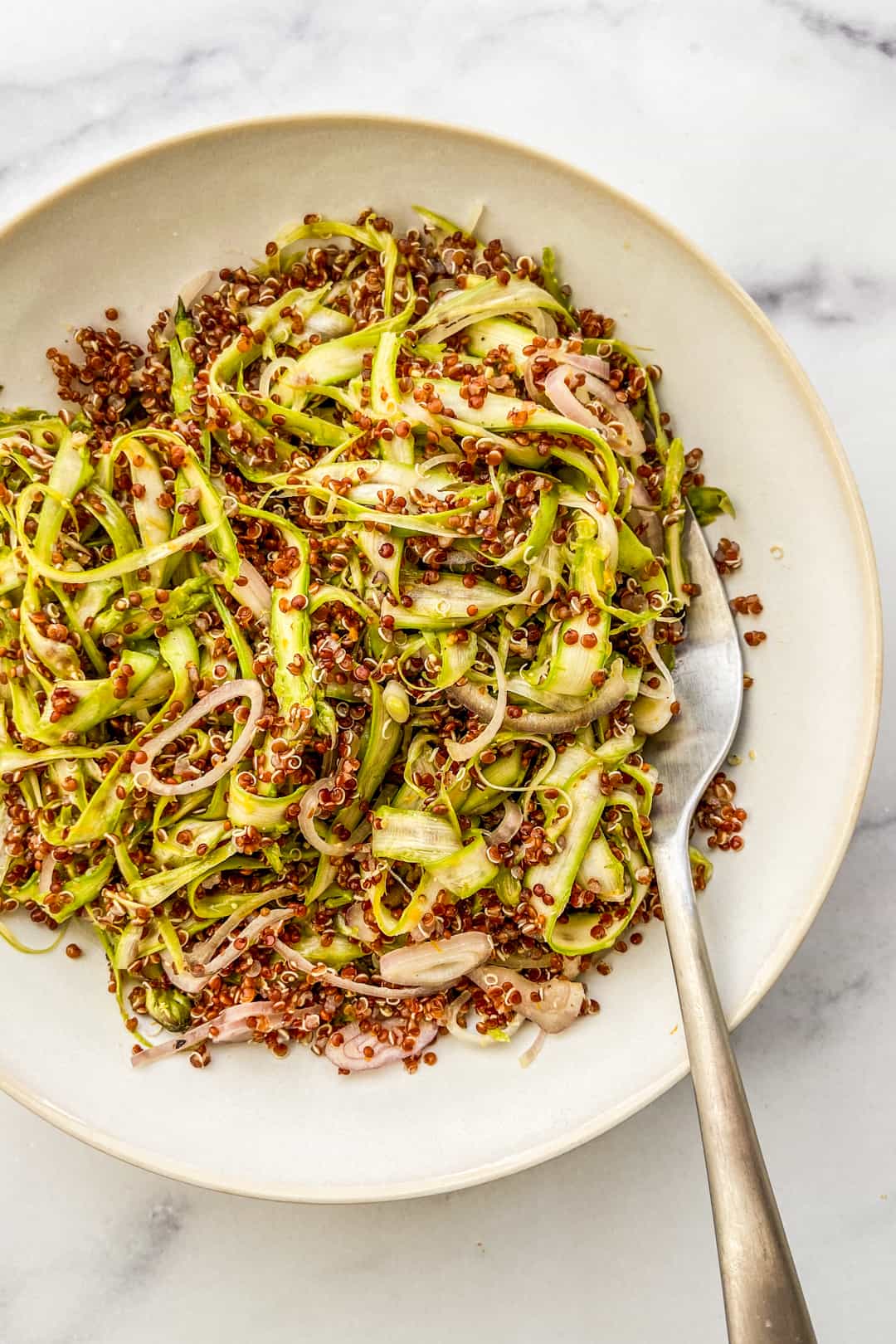 Shaved asparagus and quinoa salad in a white bowl with a spoon.