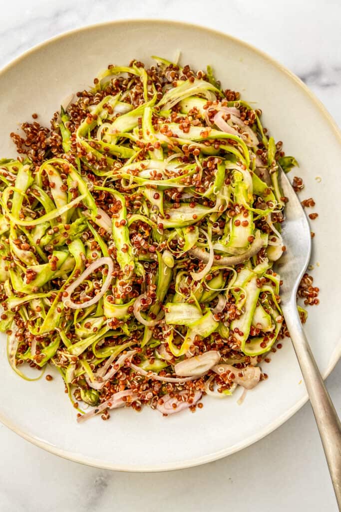 Shaved asparagus and quinoa salad in a white bowl with a spoon.