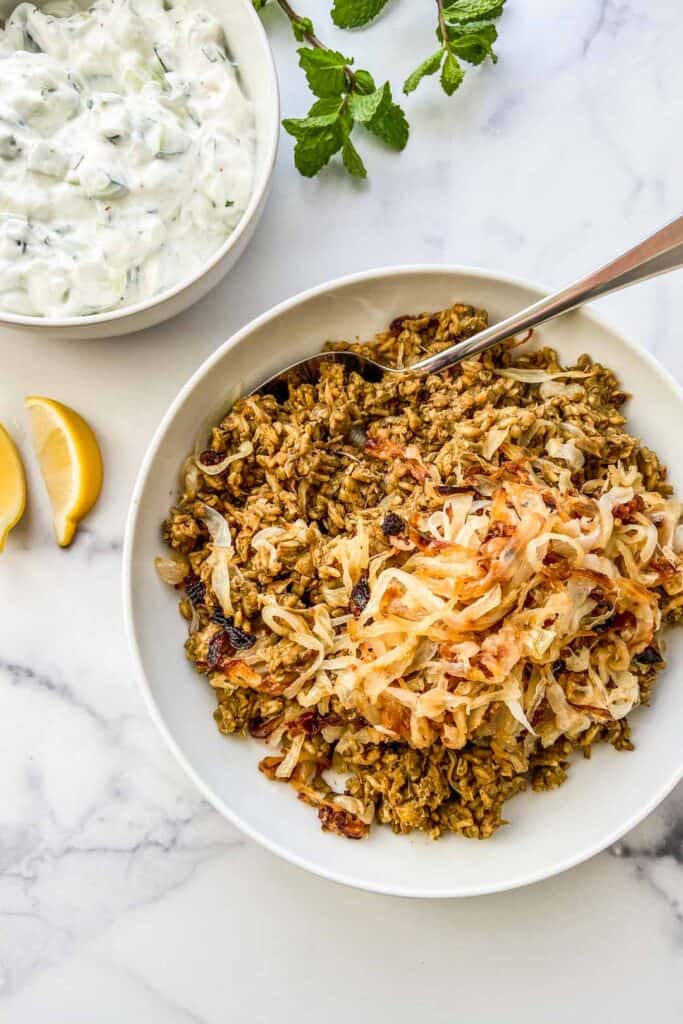 A large bowl of mujaddara next to a bowl of yogurt sauce and sliced lemons. 