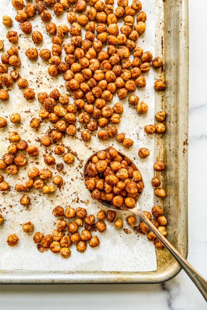 An overhead shot of chickpeas on a sheet pan with a large spoon.