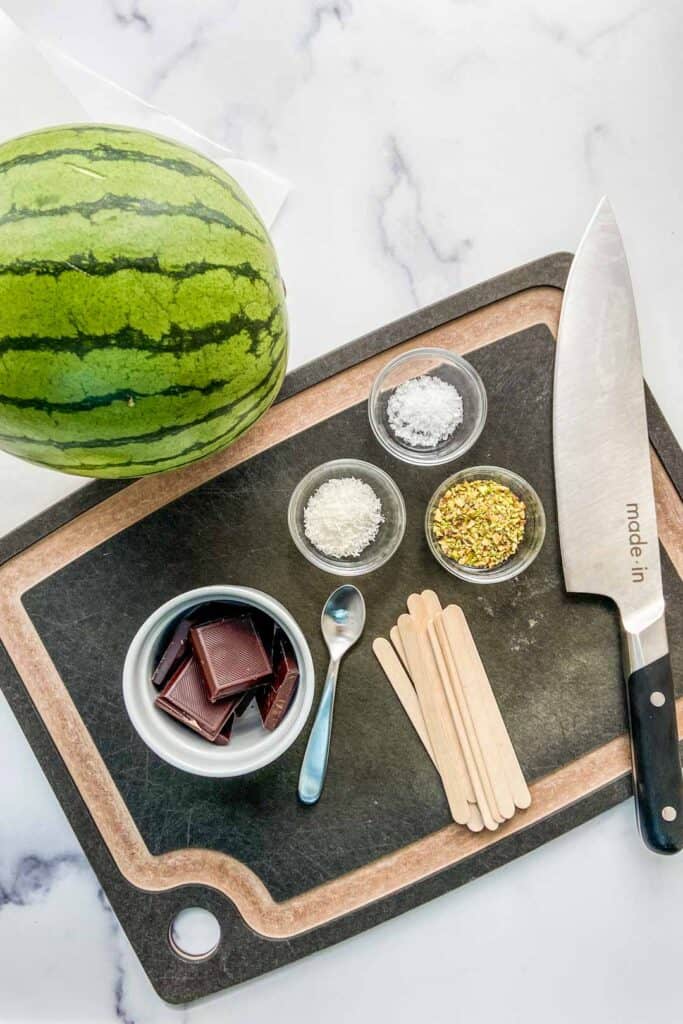 Ingredients for dark chocolate watermelon sticks on a marble background.