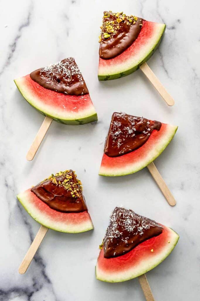 Watermelon triangles on popsicle sticks dipped in dark chocolate and topped with sea salt, pistachios, and coconut flakes.