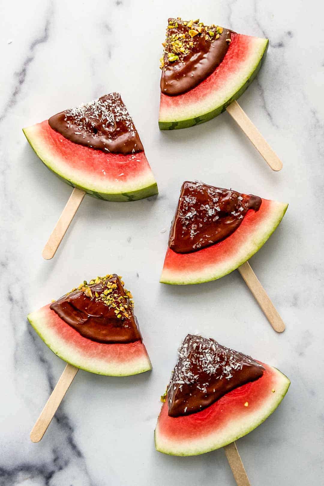 Watermelon triangles on popsicle sticks dipped in dark chocolate and topped with sea salt, pistachios, and coconut flakes.