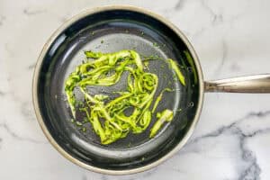 Shaved asparagus and chives in a frying pan.