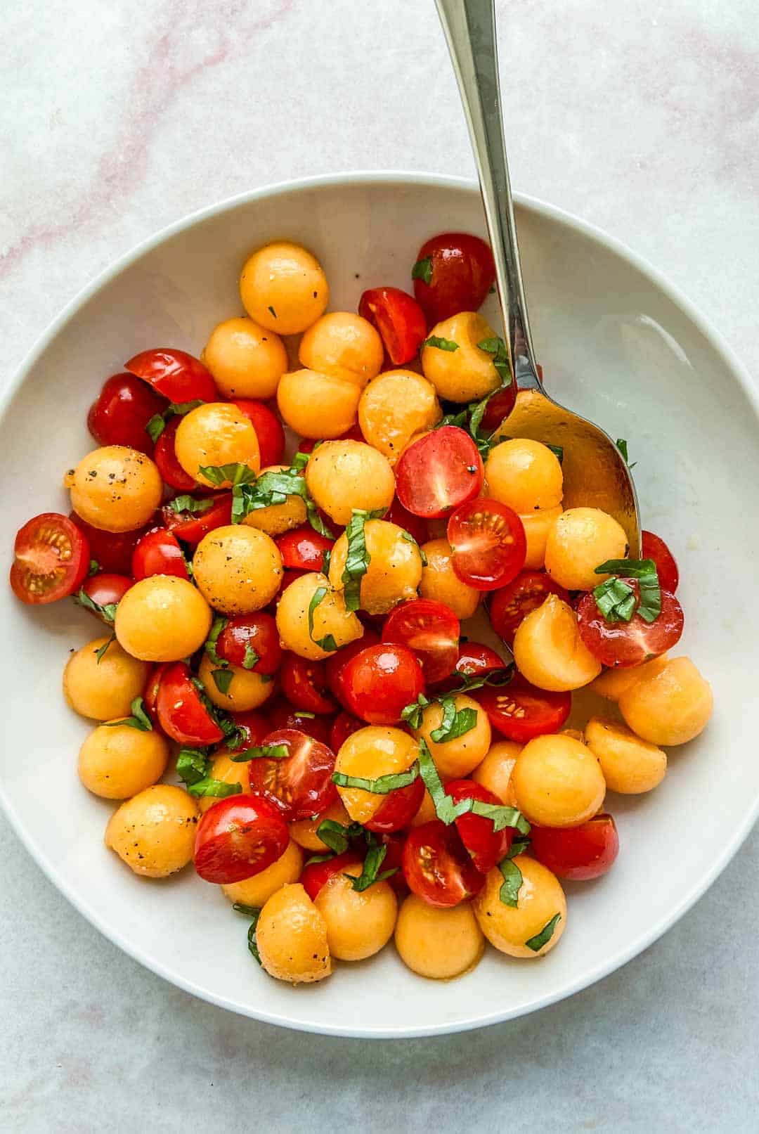 A cherry tomato and cantaloupe salad in a white bowl.