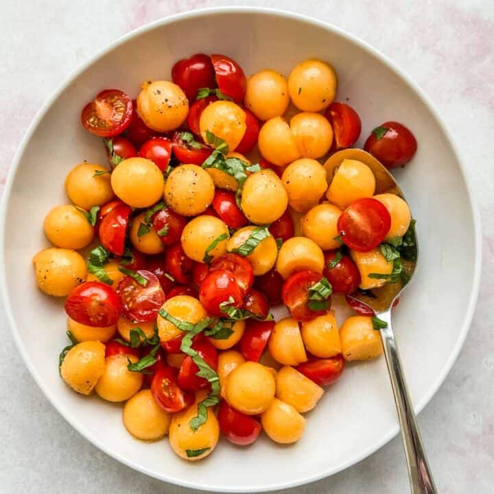 cherry tomato and cantaloupe salad in a white serving bowl with a spoon