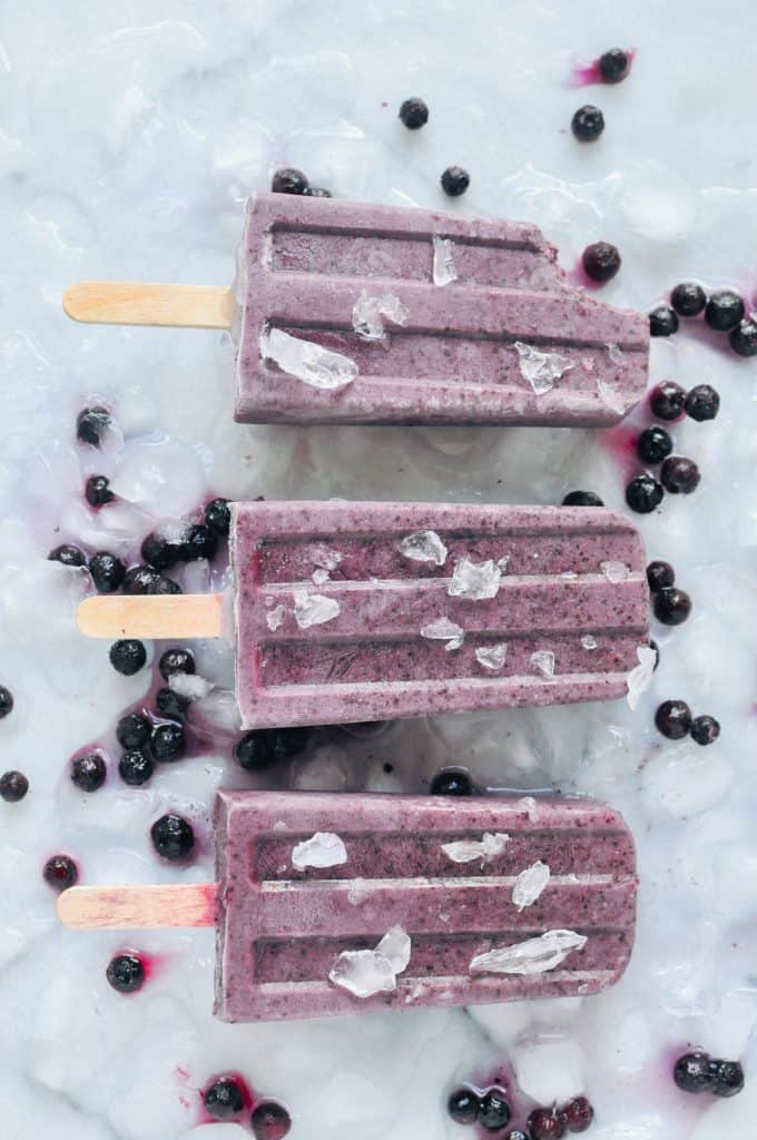 blueberry basil popsicles on a bed of crushed ice and blueberries