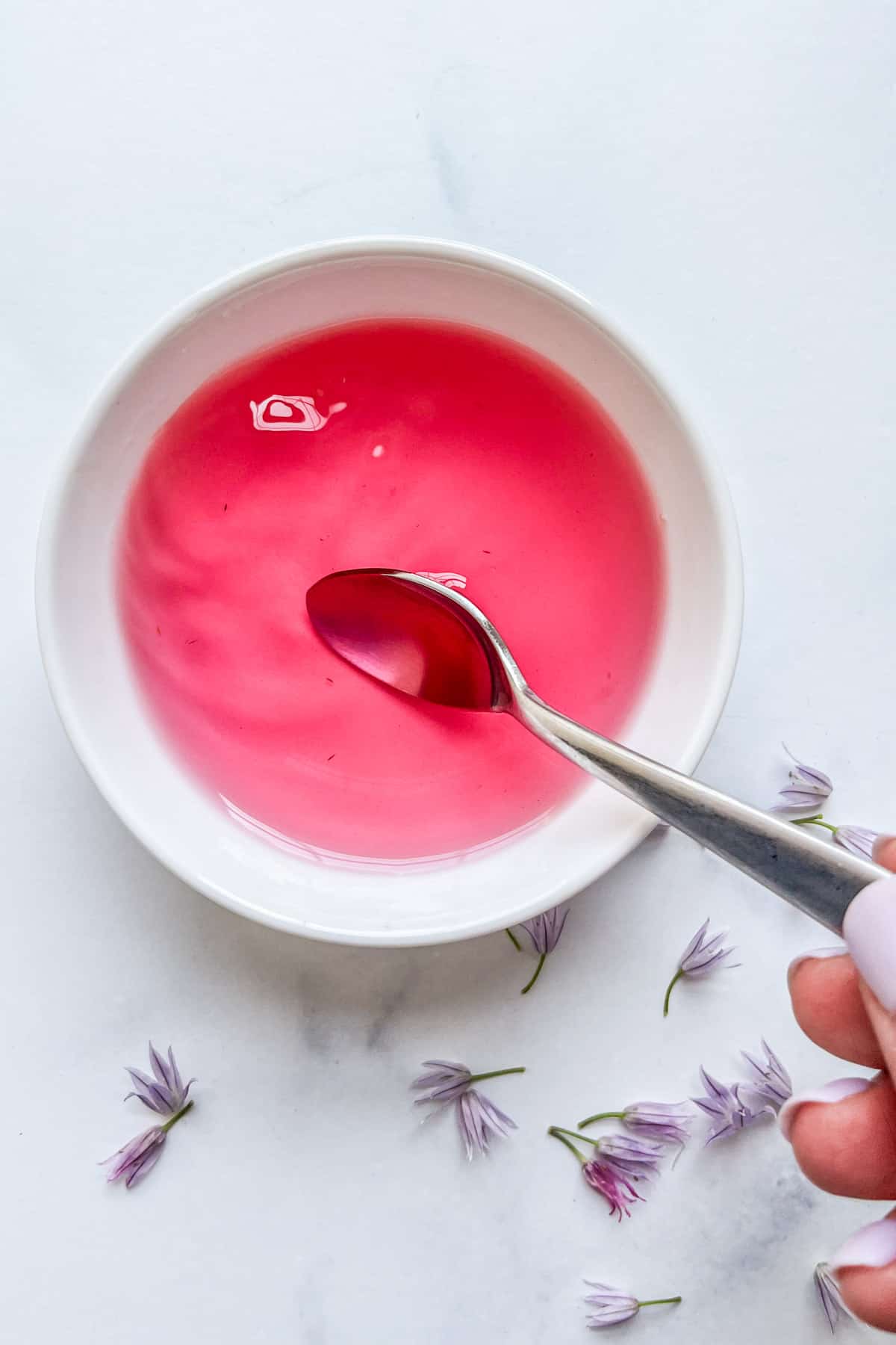 A small white bowl with chive blossom vinegar and a silver spoon.