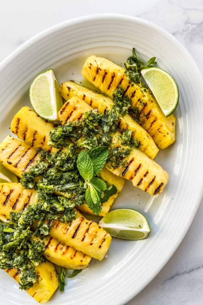 An overhead shot of grilled pineapple with lime mint sauce on a white serving dish.