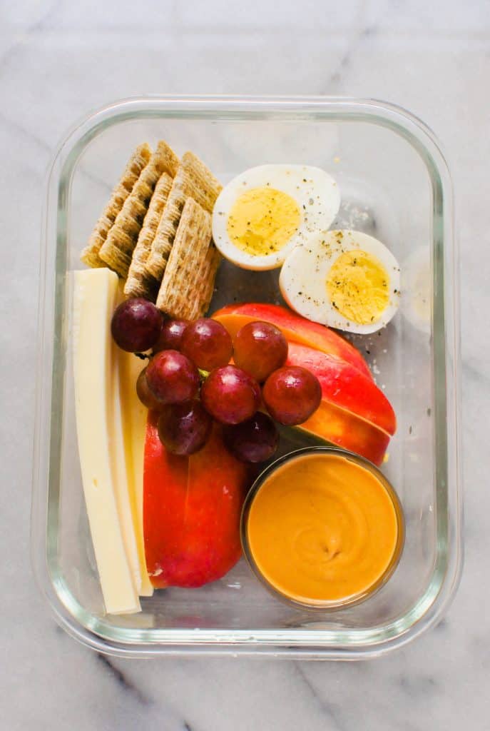 egg, grapes, apple, peanut butter, and crackers in a glass container