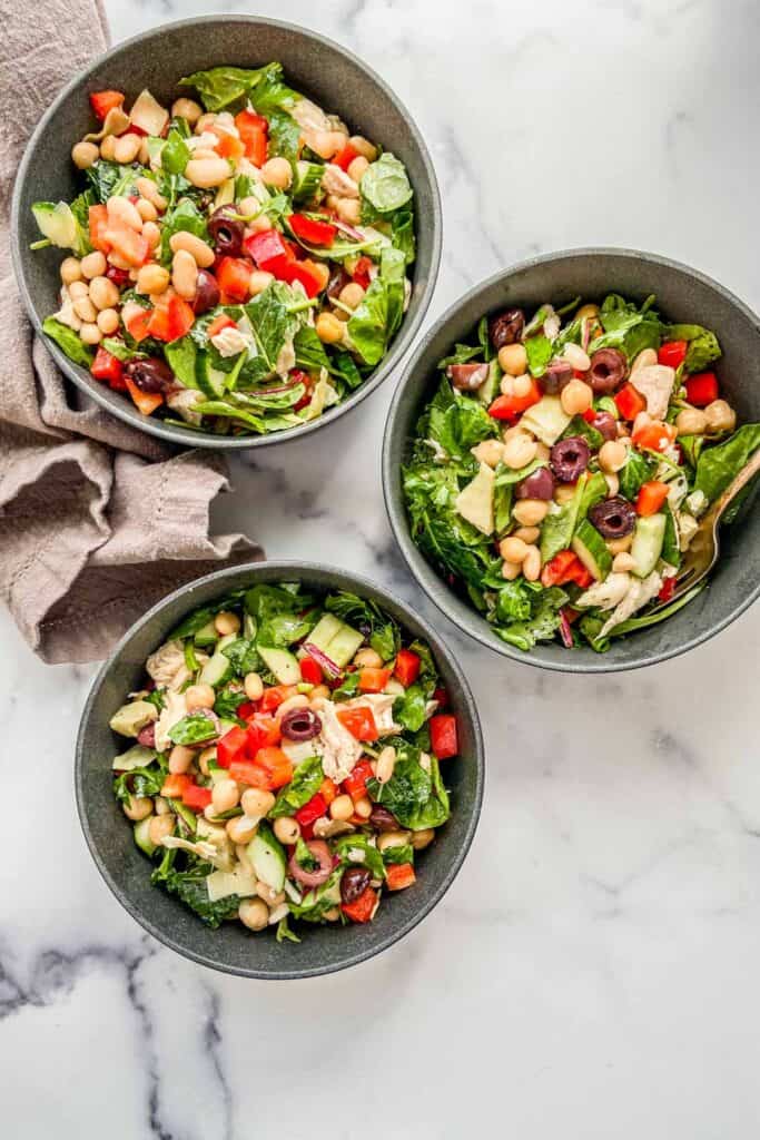 An overhead shot of three bowls of Mediterranean chicken salad.