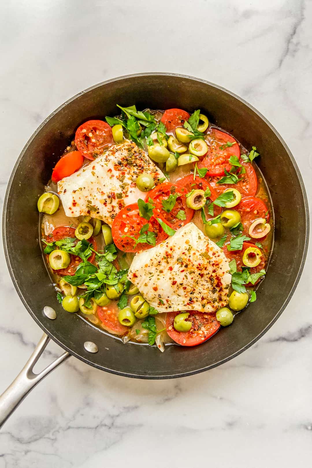 Poached sea bass with tomatoes and olives in a skillet.