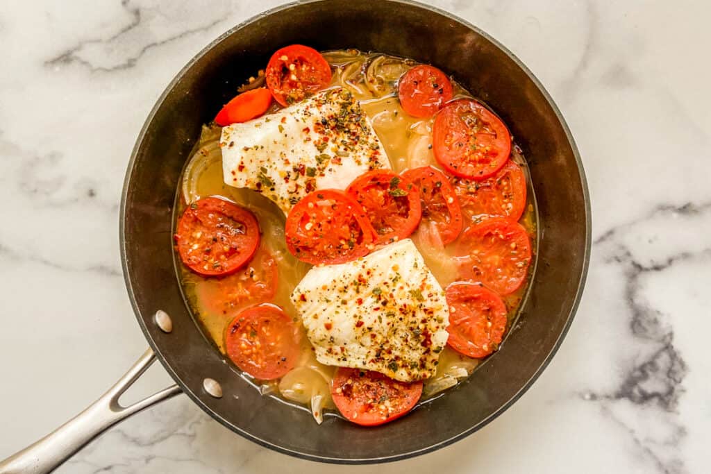 Poached sea bass and roma tomatoes in a skillet.