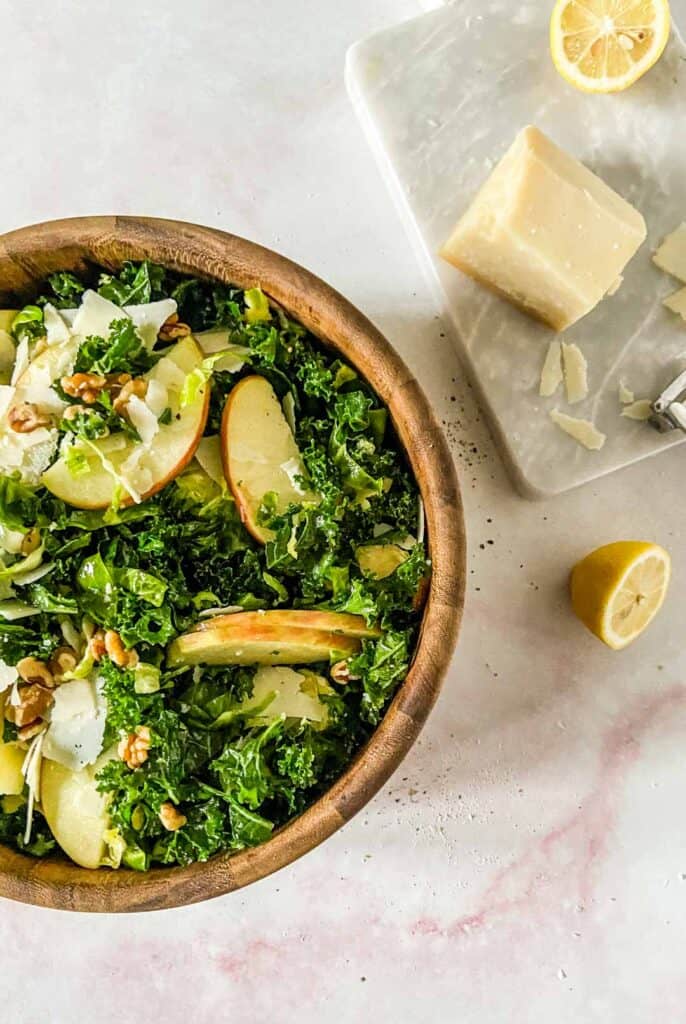 kale and brussels sprout salad in a bowl next to a cutting board with parmesan cheese