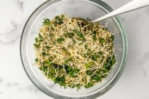 Breadcrumbs, parmesan, and parsley mixed in a glass bowl with a silver spoon.