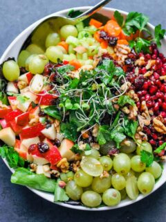 Detox salad with fruit and greens in a large white bowl.
