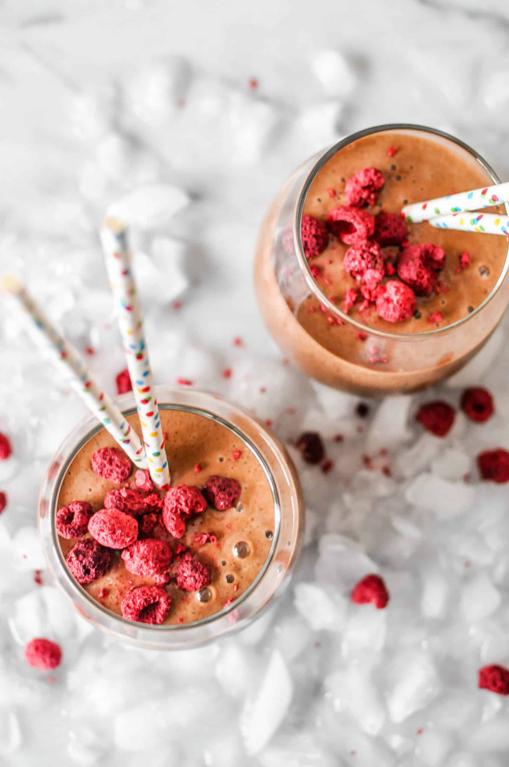 two glasses fo vegan chocolate shake topped with freeze dried raspberries