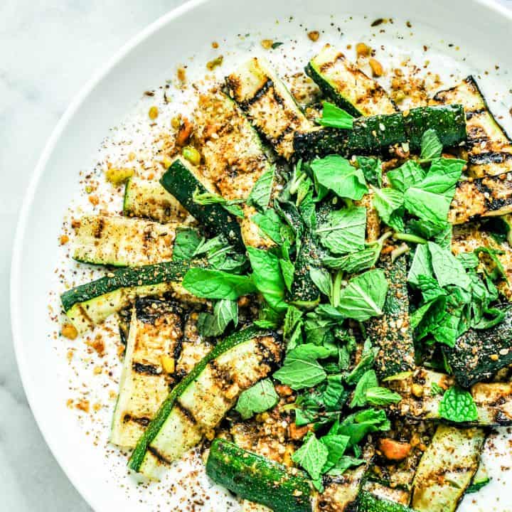 Grilled zucchini with yogurt, Dukkah, and Sumac with basil on top.