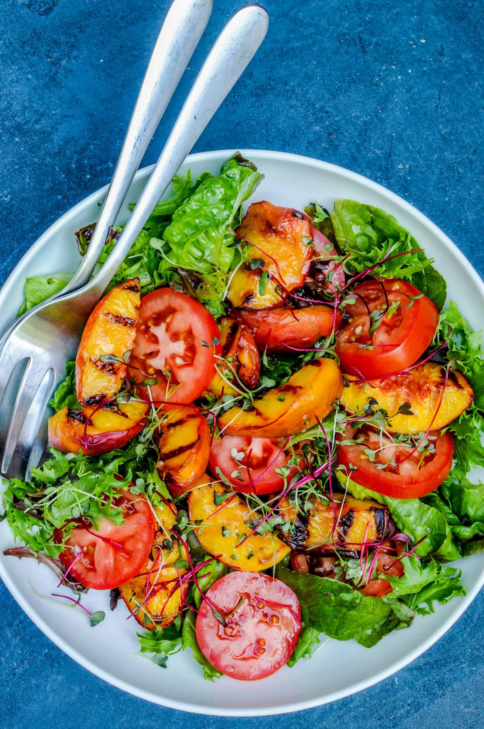 Grilled peach and tomato salad in a white bowl on a blue background.