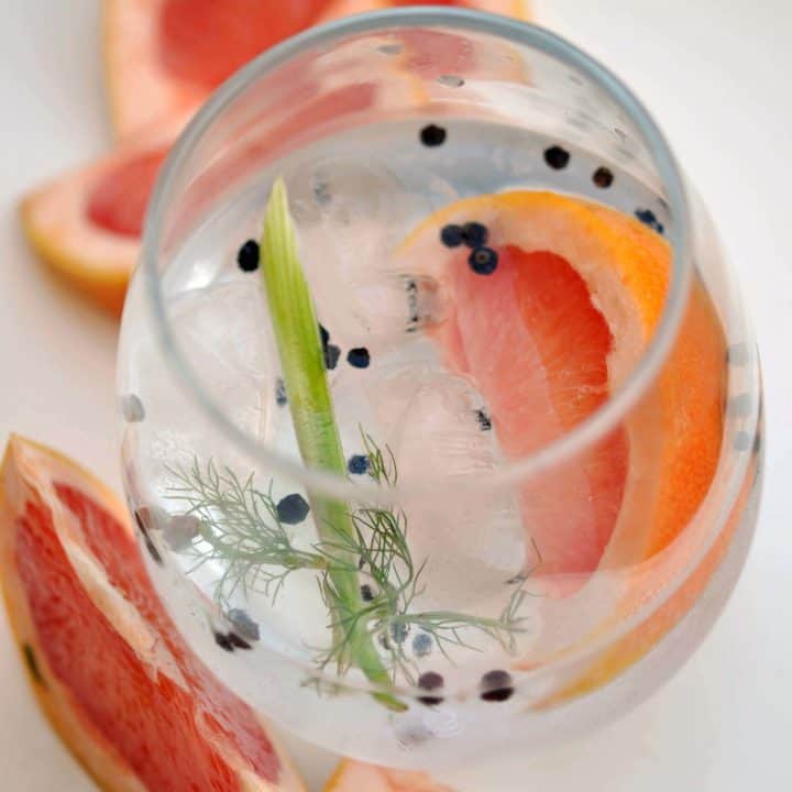 A wine glass with a gin and tonic with grapefruit, fennel, and black peppercorns.