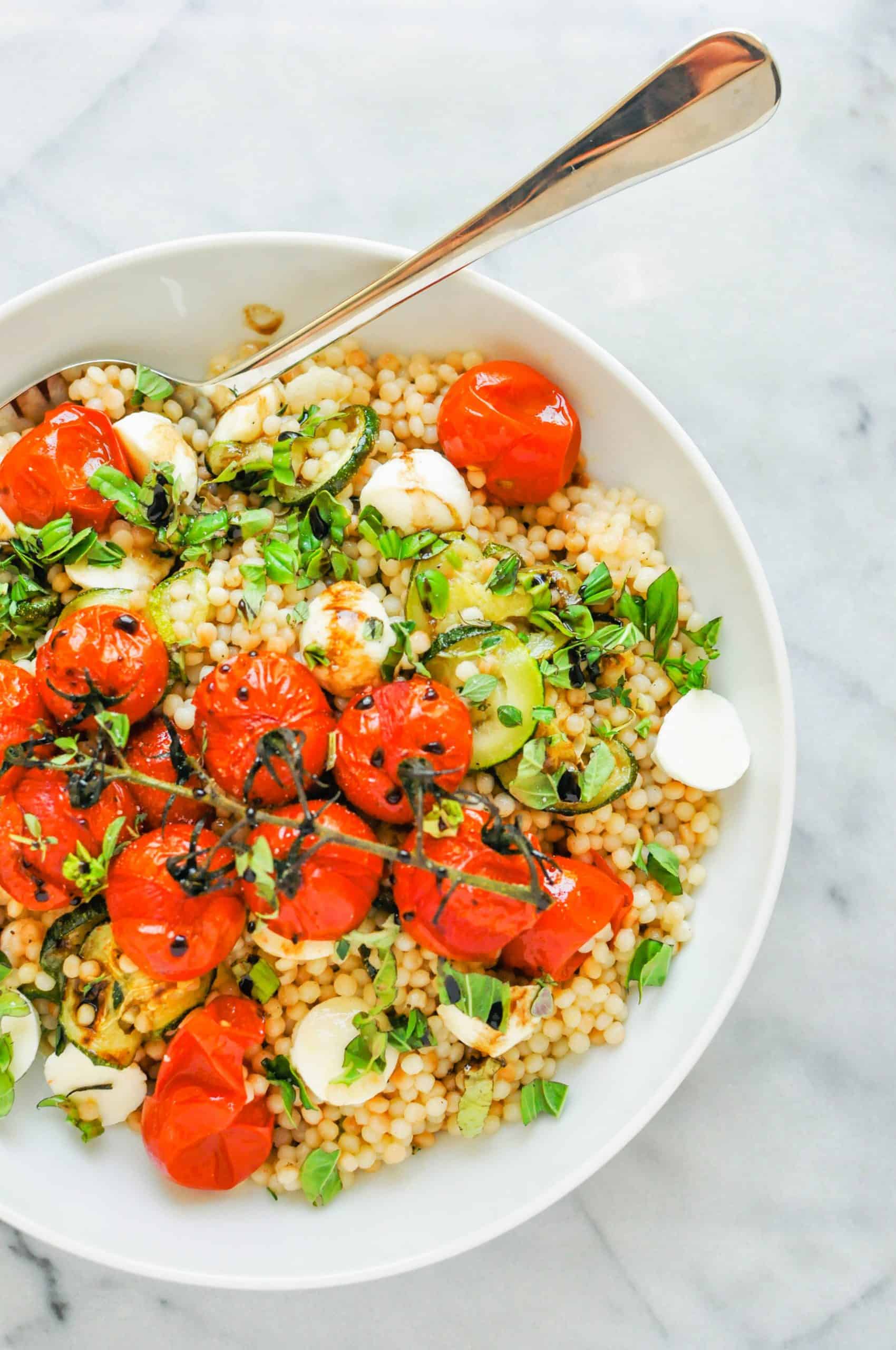 Pearl couscous salad with tomatoes and zucchini in a white bowl.