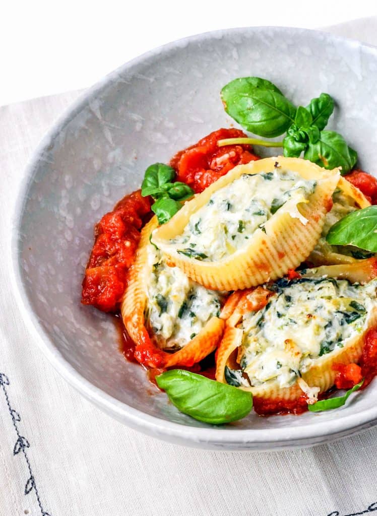 Spinach artichoke stuffed shells in a white bowl.