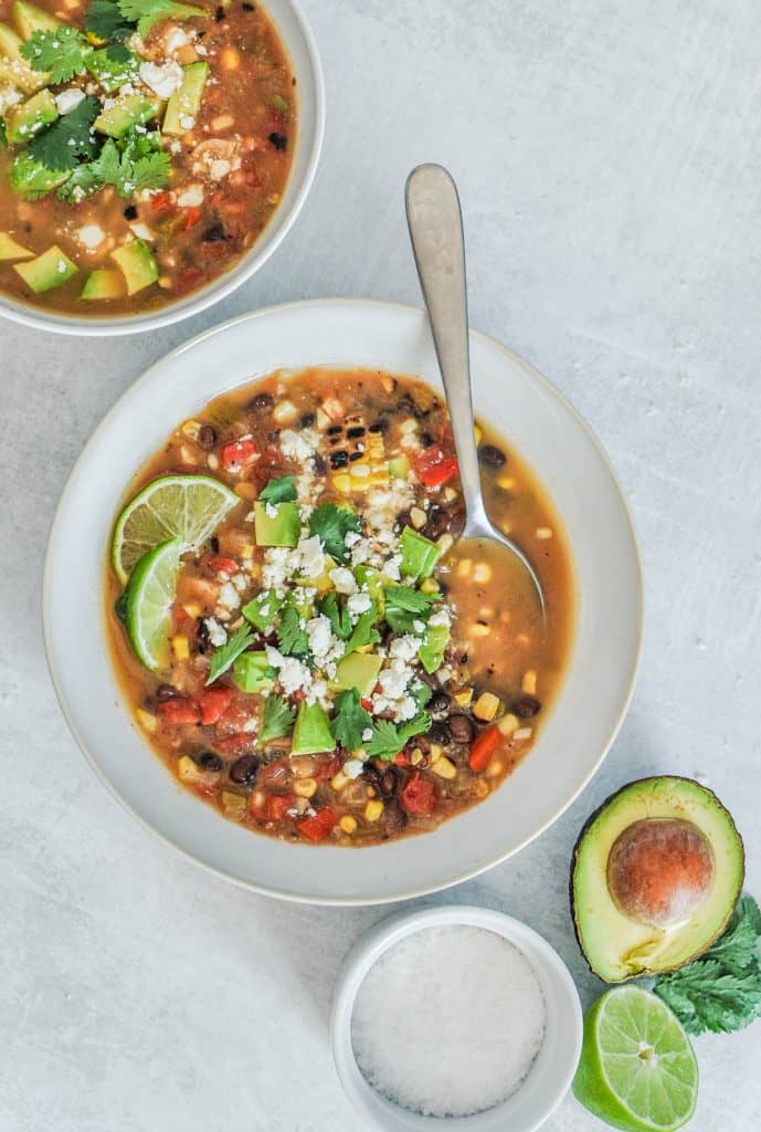 Mexican veggie soup in a white bowl with a side of avocado