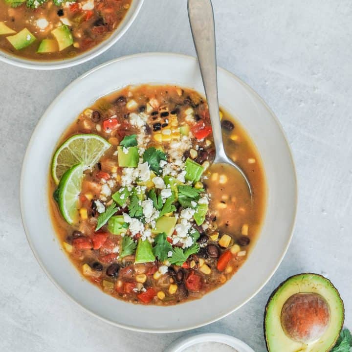 Mexican veggie soup in a white bowl with a side of avocado