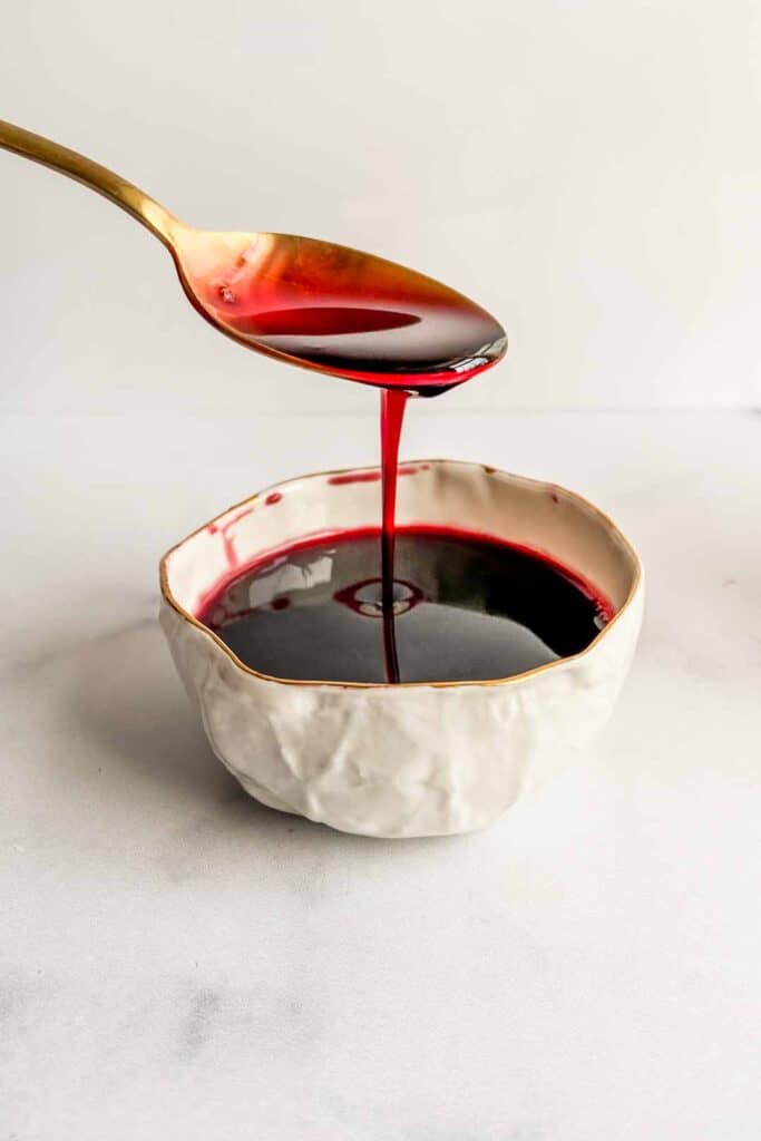 Pomegranate molasses dripping from a spoon into a small bowl.