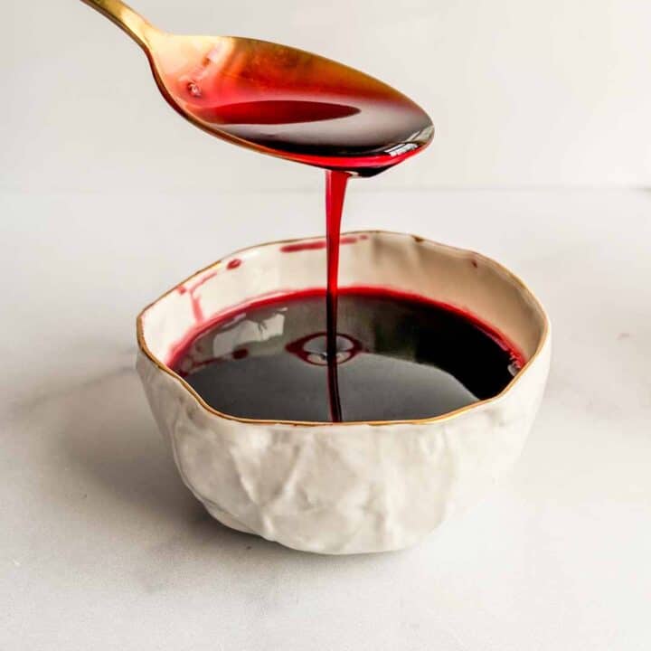 Pomegranate molasses dripping from a spoon into a small bowl.