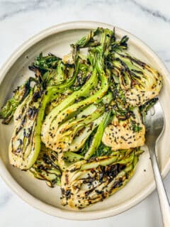 An overhead shot of a bowl of grilled baby bok choy, topped with sesame seeds.