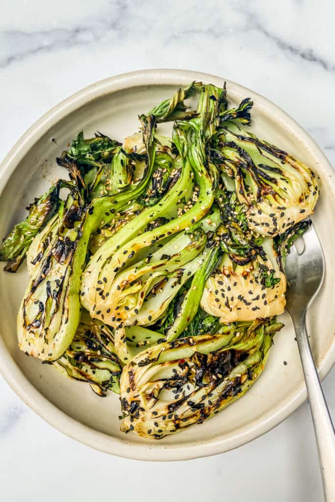 An overhead shot of a bowl of grilled baby bok choy, topped with sesame seeds.