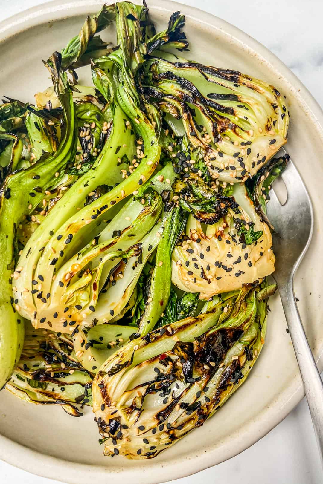 A closeup shot of a bowl of grilled baby bok choy with a silver spoon.