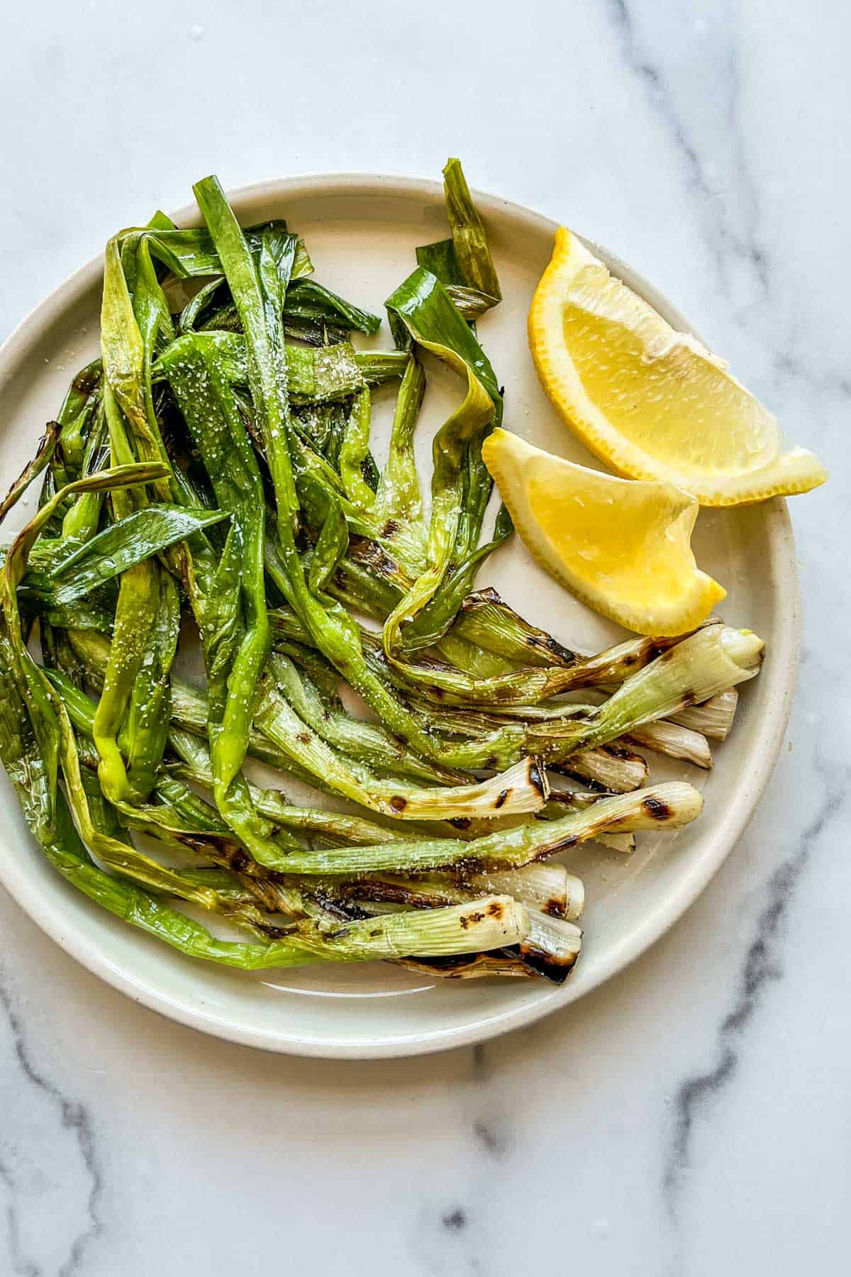 Grilled scallions with lemon slices on a white plate.