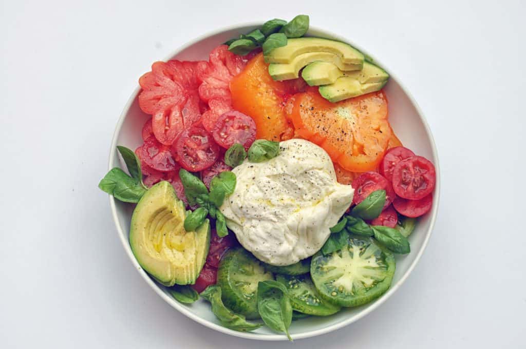 heirloom tomatoes, burrata, basil, and avocado on a plate