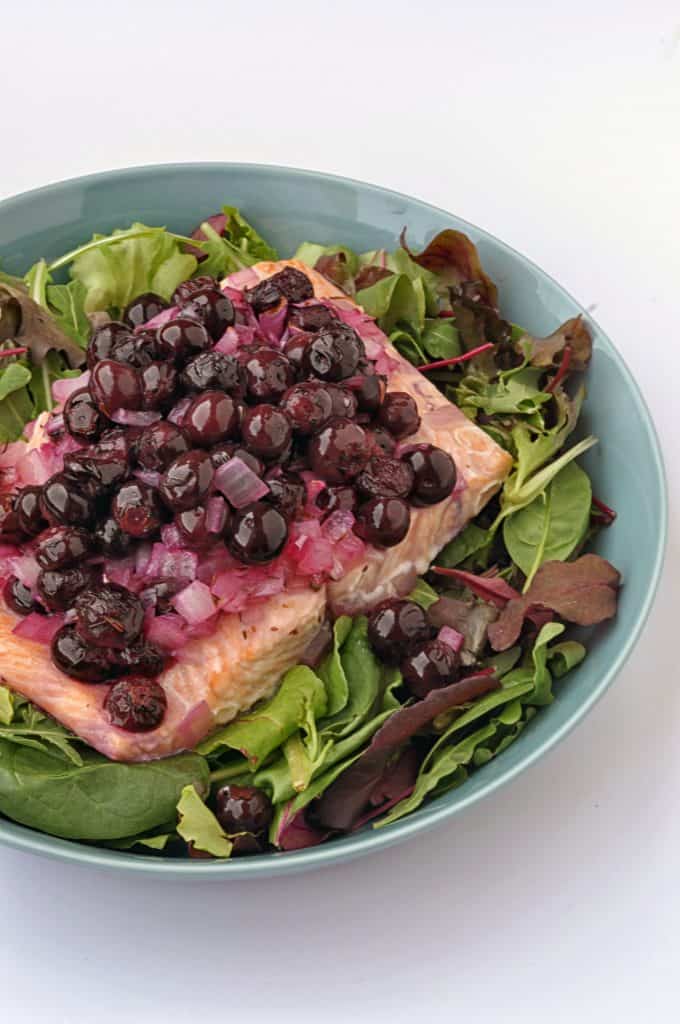 salmon with blueberries on a plate with greens