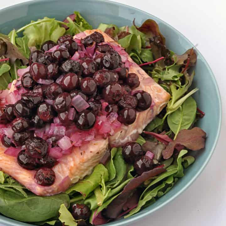 salmon with blueberries on a plate with greens