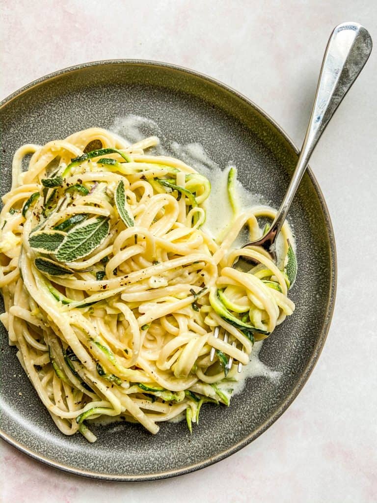 Creamy zucchini pasta on a grey plate with a fork.