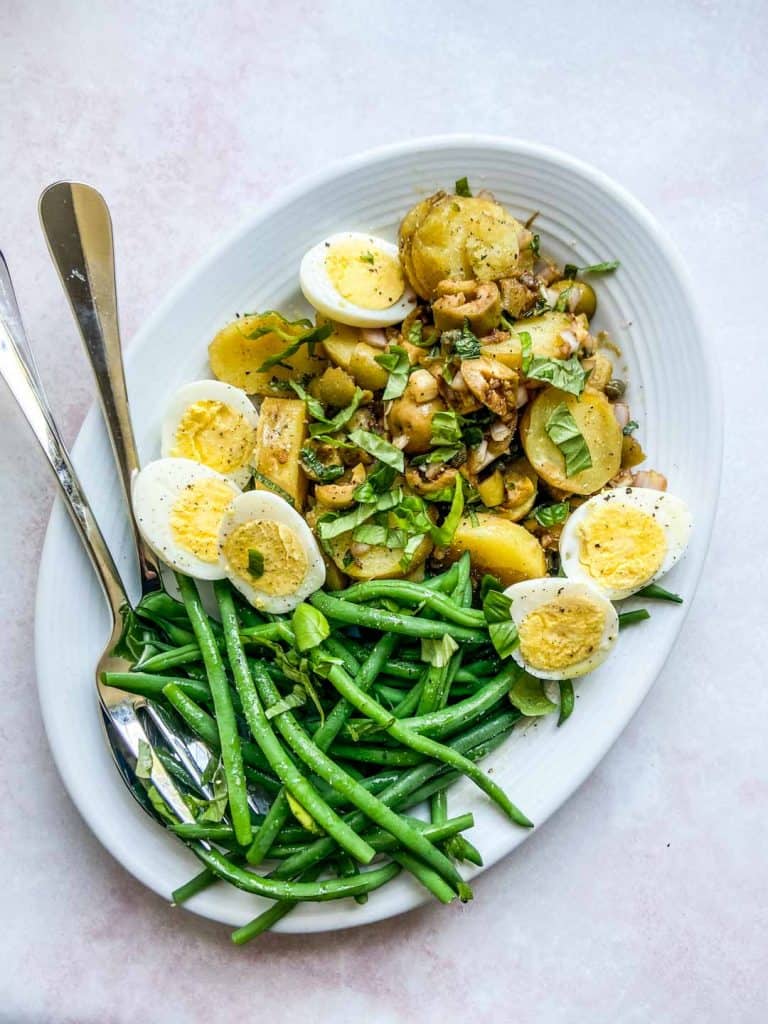 French potato salad on a white platter with serving spoons