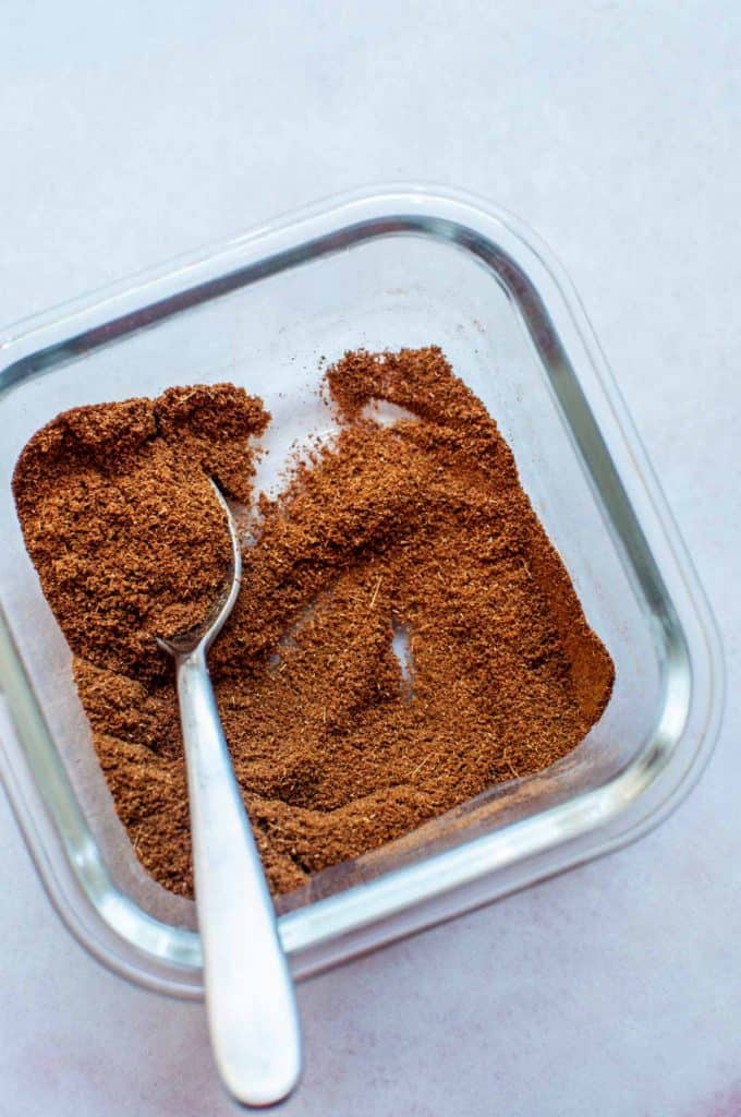 Chinese five spice powder in a small glass container, with a small spoon