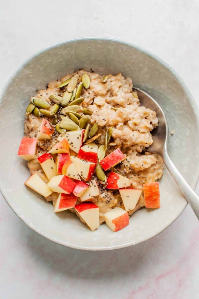 pumpkin spice oatmeal in a bowl, topped with pepitas and apples chunks