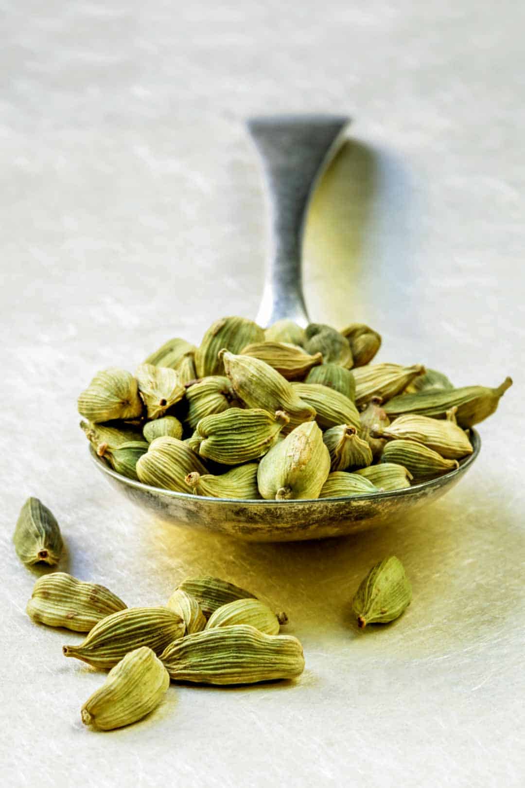 A spoon holding cardamom pods.