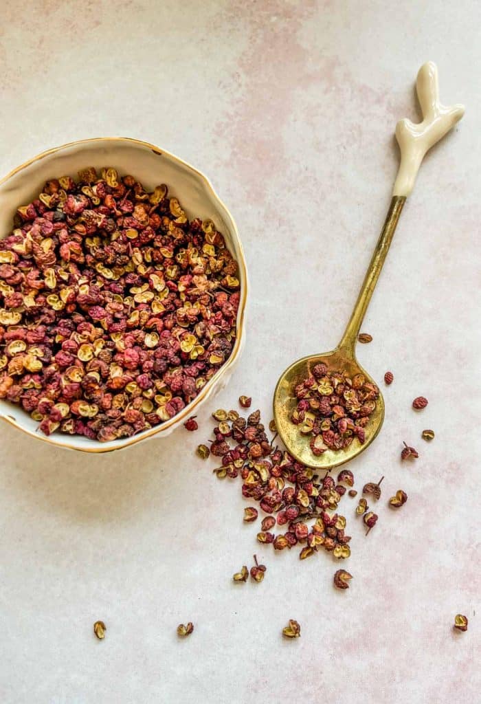 sichuan peppercorns on a gold spoon and in a small white bowl