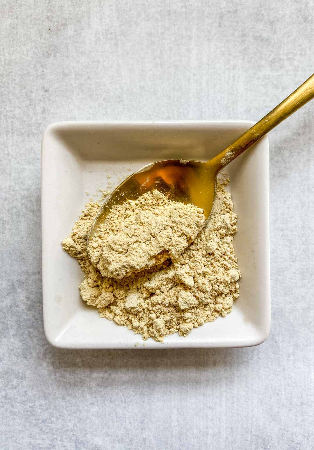 Fenugreek spice in a small square white dish with a spoon.