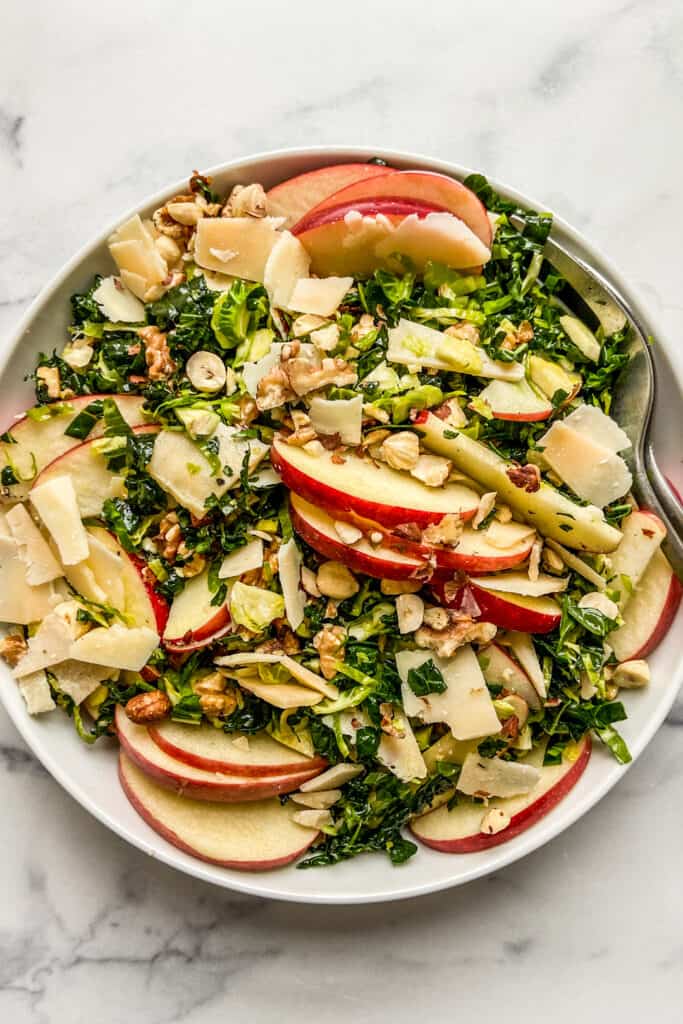 A closeup shot of a brussels sprouts kale salad in a white serving bowl.