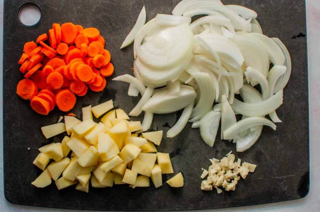chopped apple, carrots, onions, and garlic on a cutting board