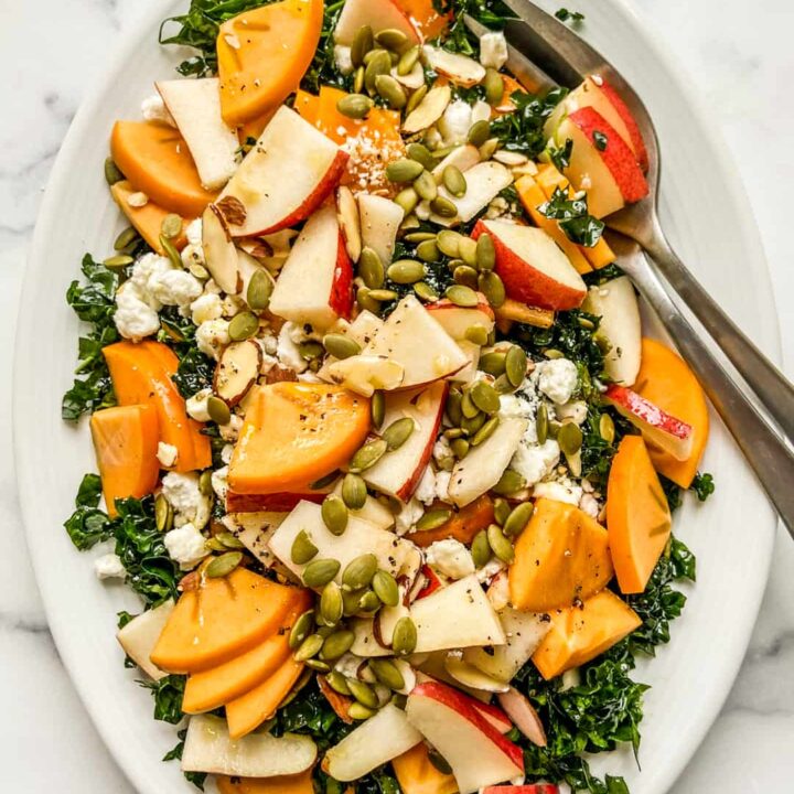 An overhead shot of a white platter with persimmon and pear salad.
