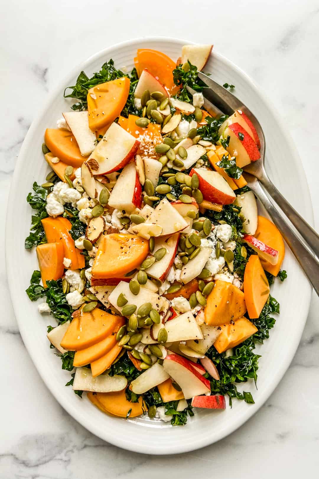 An overhead shot of a white platter with persimmon and pear salad.