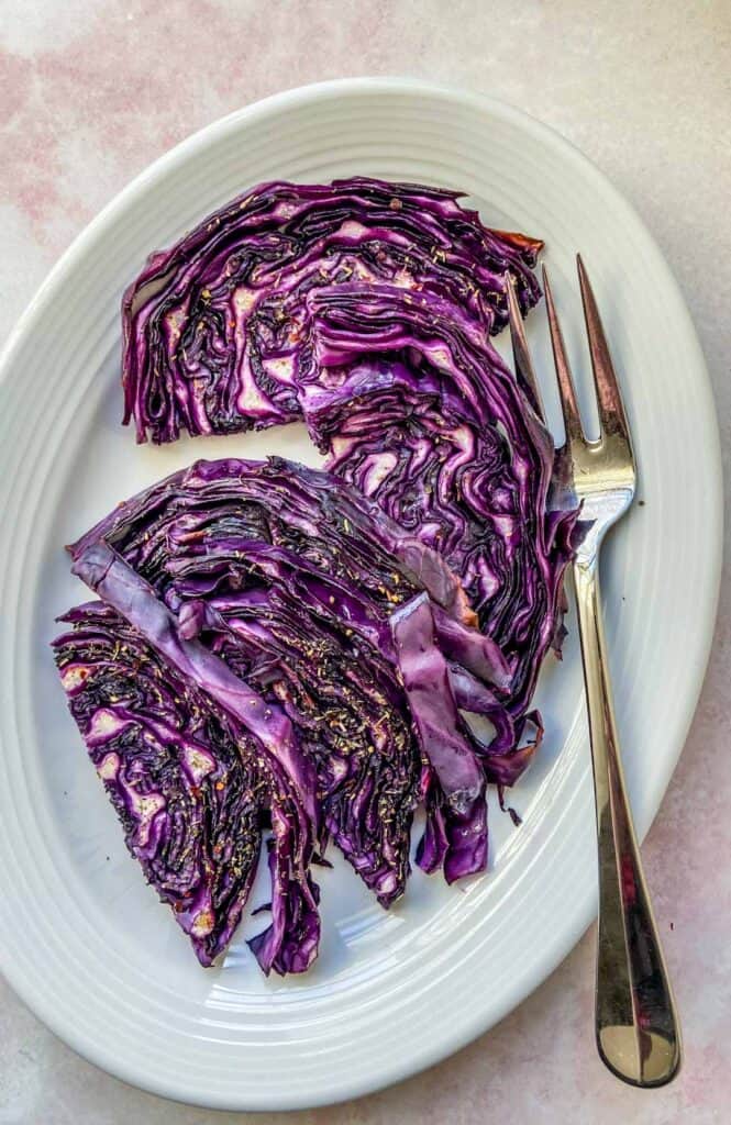 Roasted red cabbage slices on a white platter with a serving fork.