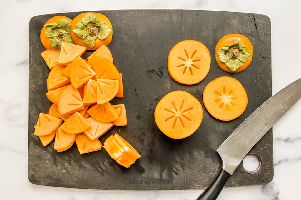 Sliced persimmons on a black cutting board with a large knife.
